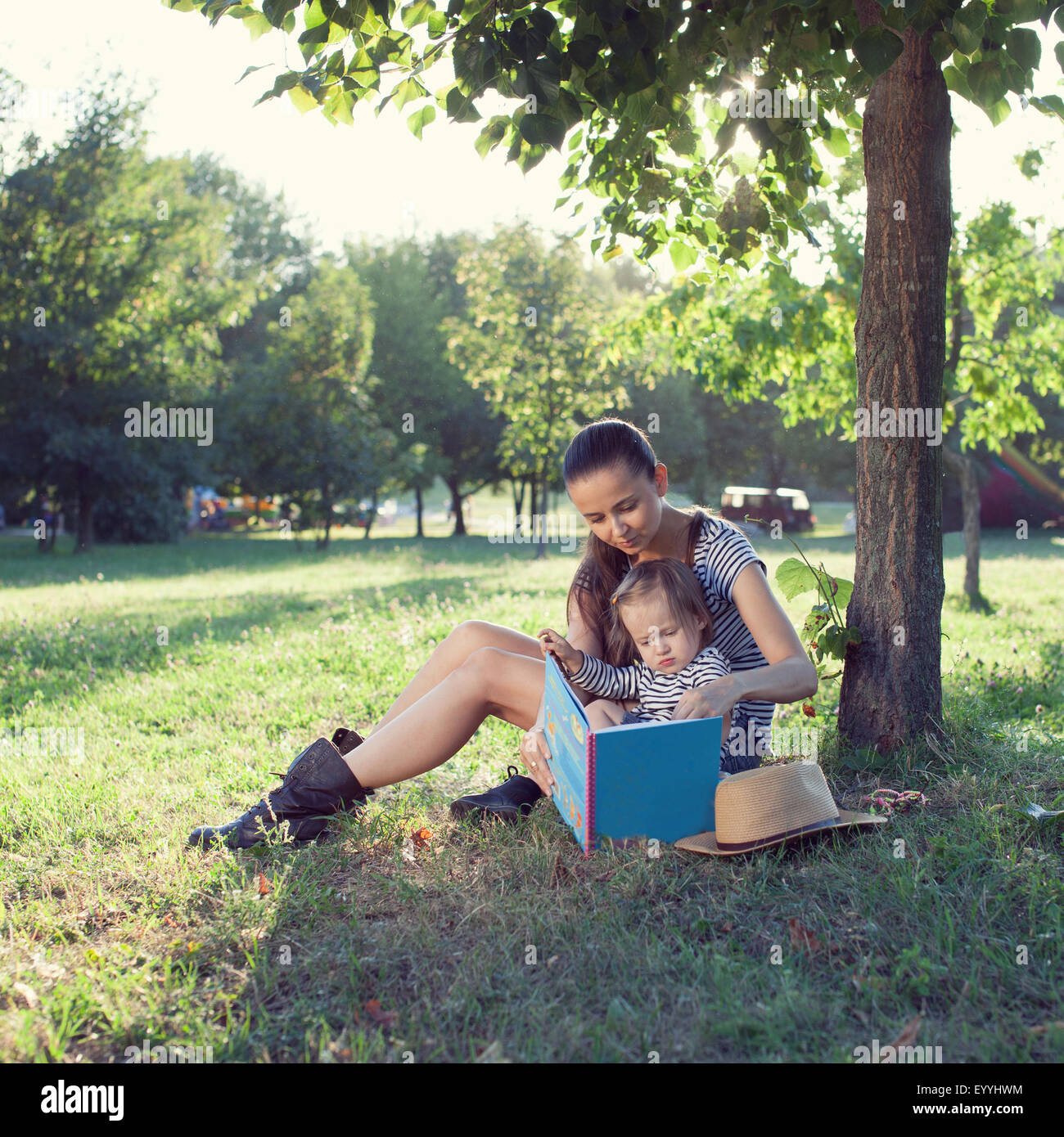 Junge stilvolle Mutter und Kleinkind Lesebuch im Garten im Sommer-Spaß Stockfoto