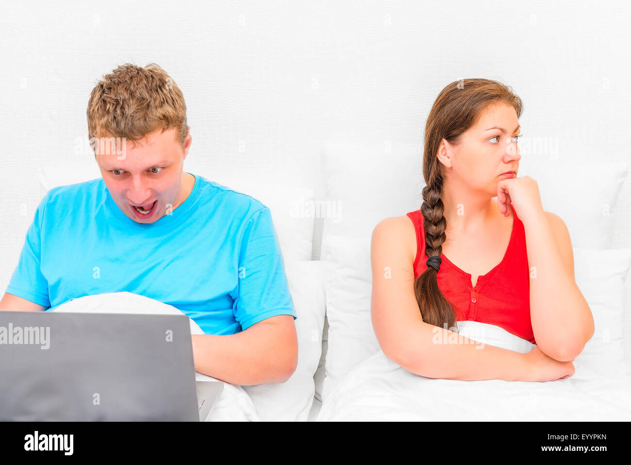 ein Mann mit einem Laptop und eine frustrierte Frau im Bett Stockfoto