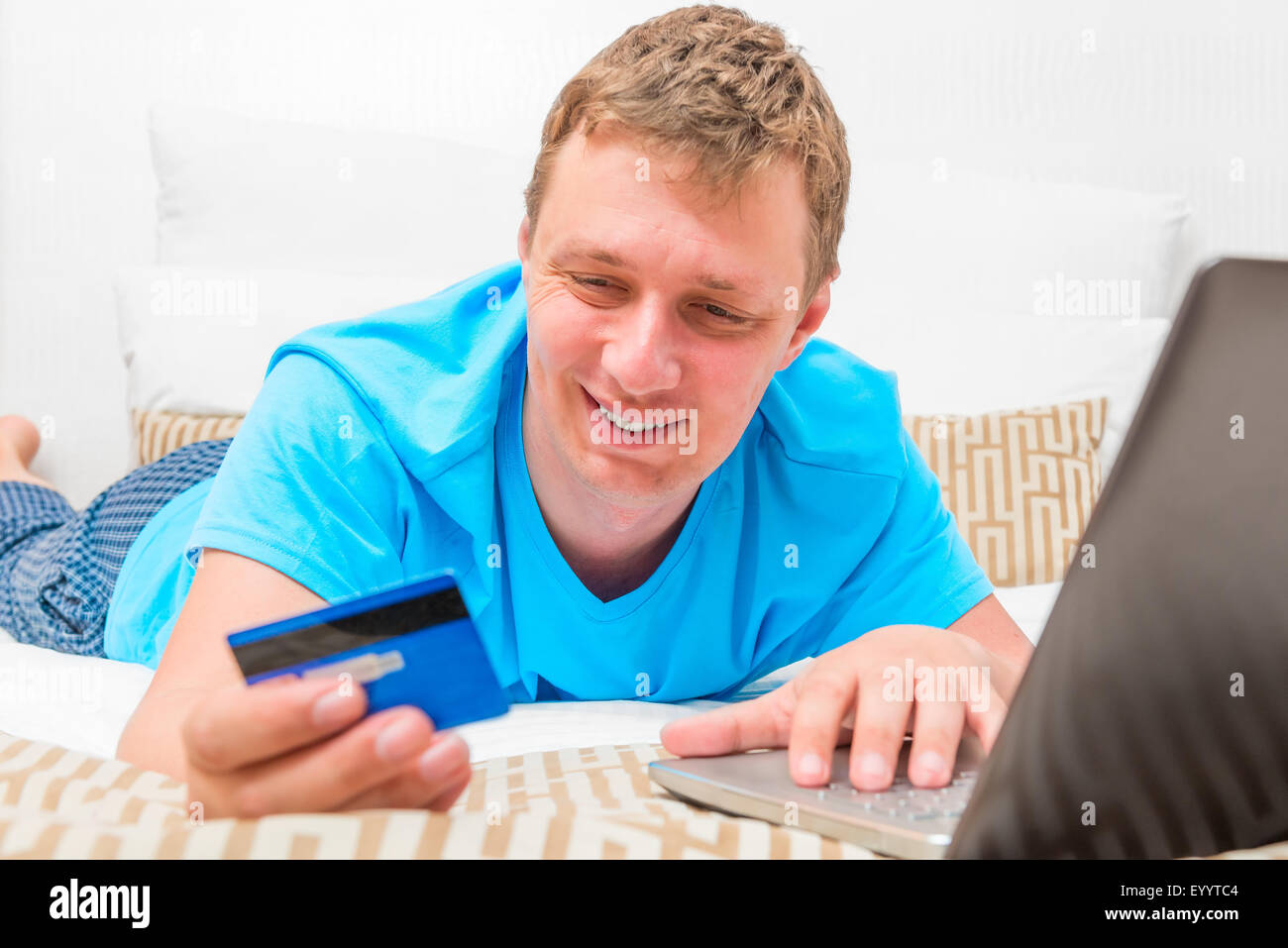 Glücklicher Mann mit einer Kreditkarte auf dem Bett Stockfoto