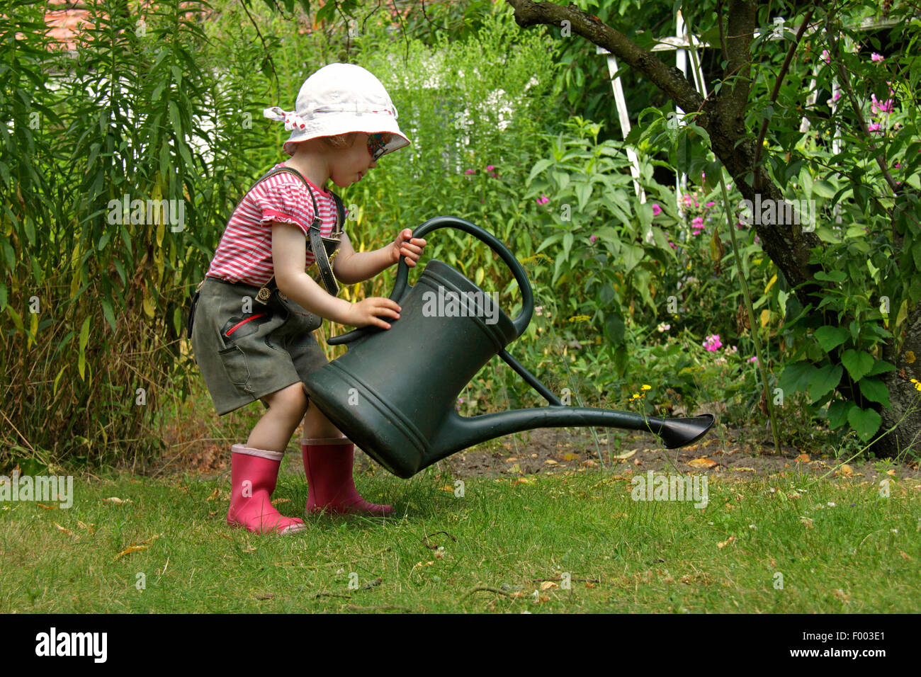 kleines Mädchen in Lederhosen spielen im Garten mit der Gießkanne, Deutschland Stockfoto