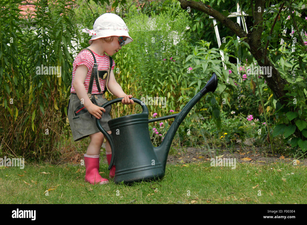 kleines Mädchen in Lederhosen spielen im Garten mit der Gießkanne, Deutschland Stockfoto