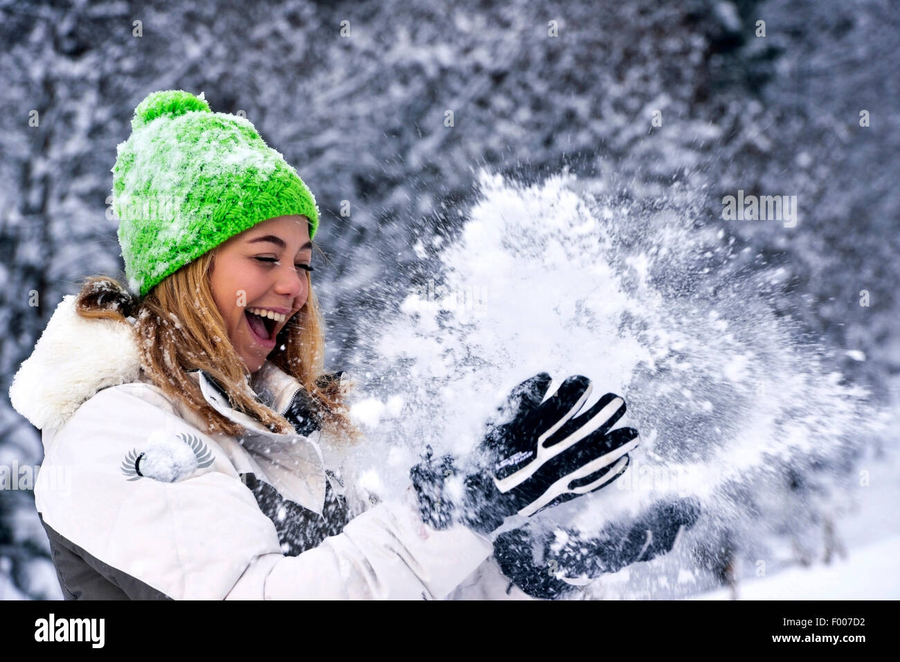 fröhliche gut aussehende junge Frau wirft Schnee, Frankreich, Savoie Stockfoto