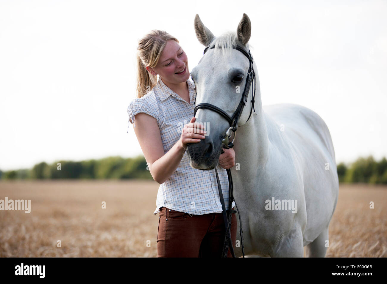 Eine junge Frau in einem Weizenfeld streicheln einen Pferde-Maulkorb Stockfoto