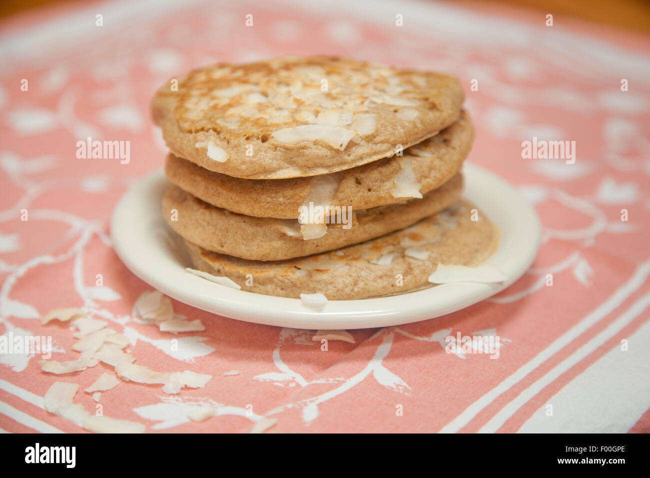 Ein Stapel von Vollkorn Kokos Pfannkuchen sitzt auf einem kleinen weißen Teller mit Pfirsich und weißen Tuch unter. Stockfoto