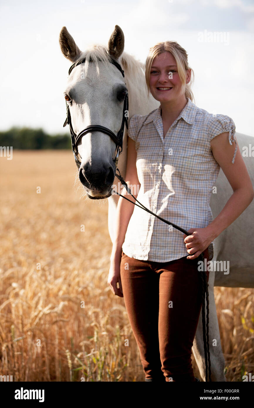 Eine junge Frau in einem Weizenfeld hält ihr Pferd Stockfoto