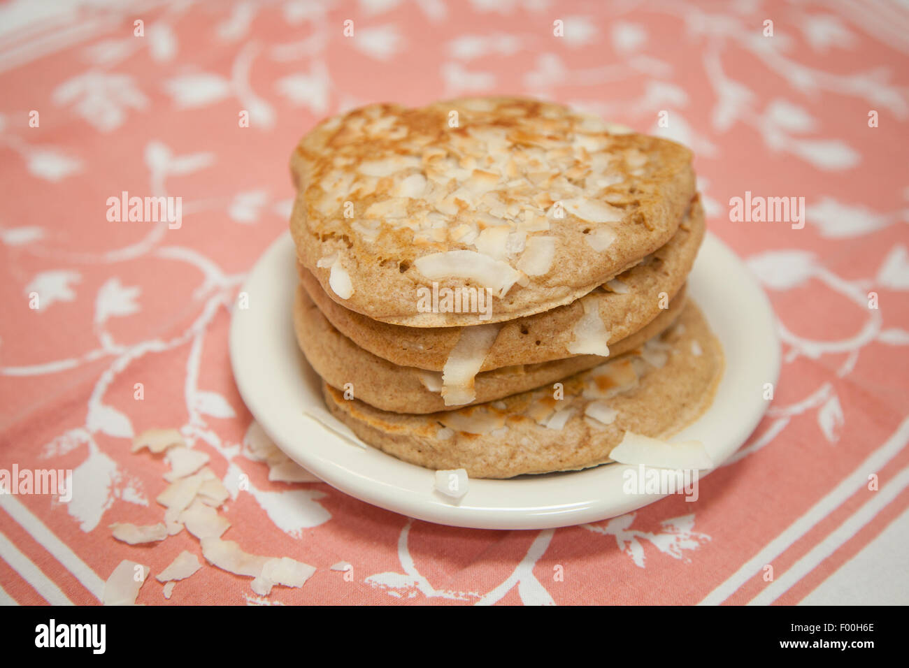 Ein Stapel von Vollkorn Kokos Pfannkuchen sitzt auf einem kleinen weißen Teller mit Pfirsich und weißen Tuch unter. Stockfoto