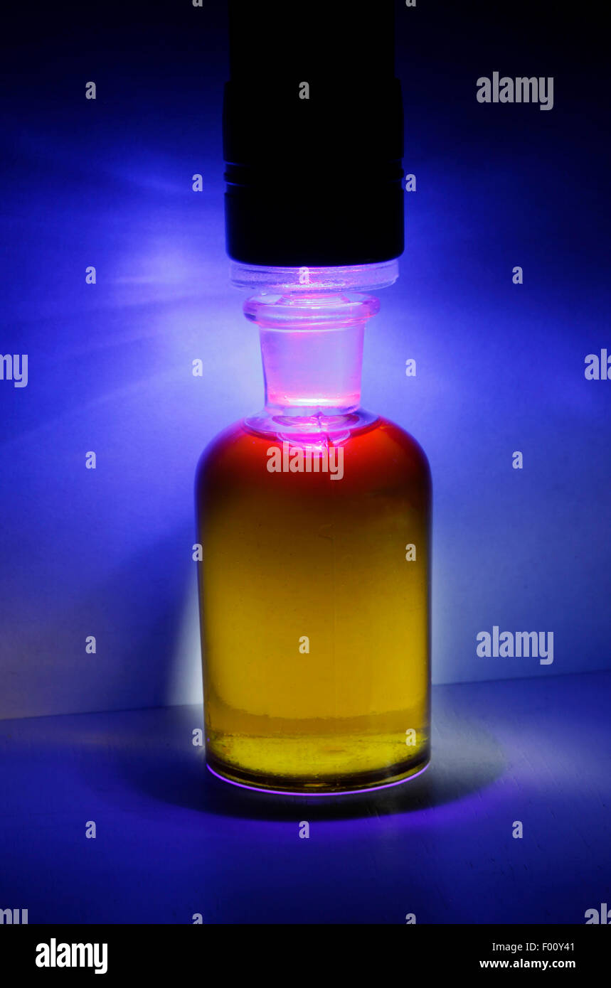 eine UV-Licht auf eine kleine Flasche extra Vergine Olivenöl, platziert strahlt nach unten in die Flüssigkeit. Stockfoto