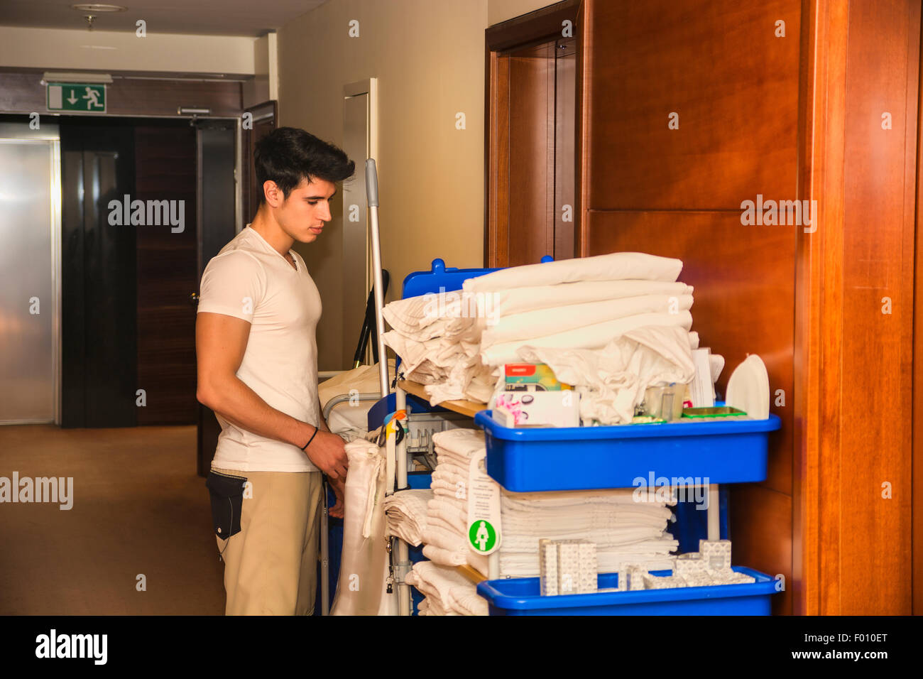 Junger Mann schob einen Haushalt Wagen beladen mit saubere Handtücher, Wäsche und Reinigungsgeräte in einem Hotel, als er das Zimmer services Stockfoto