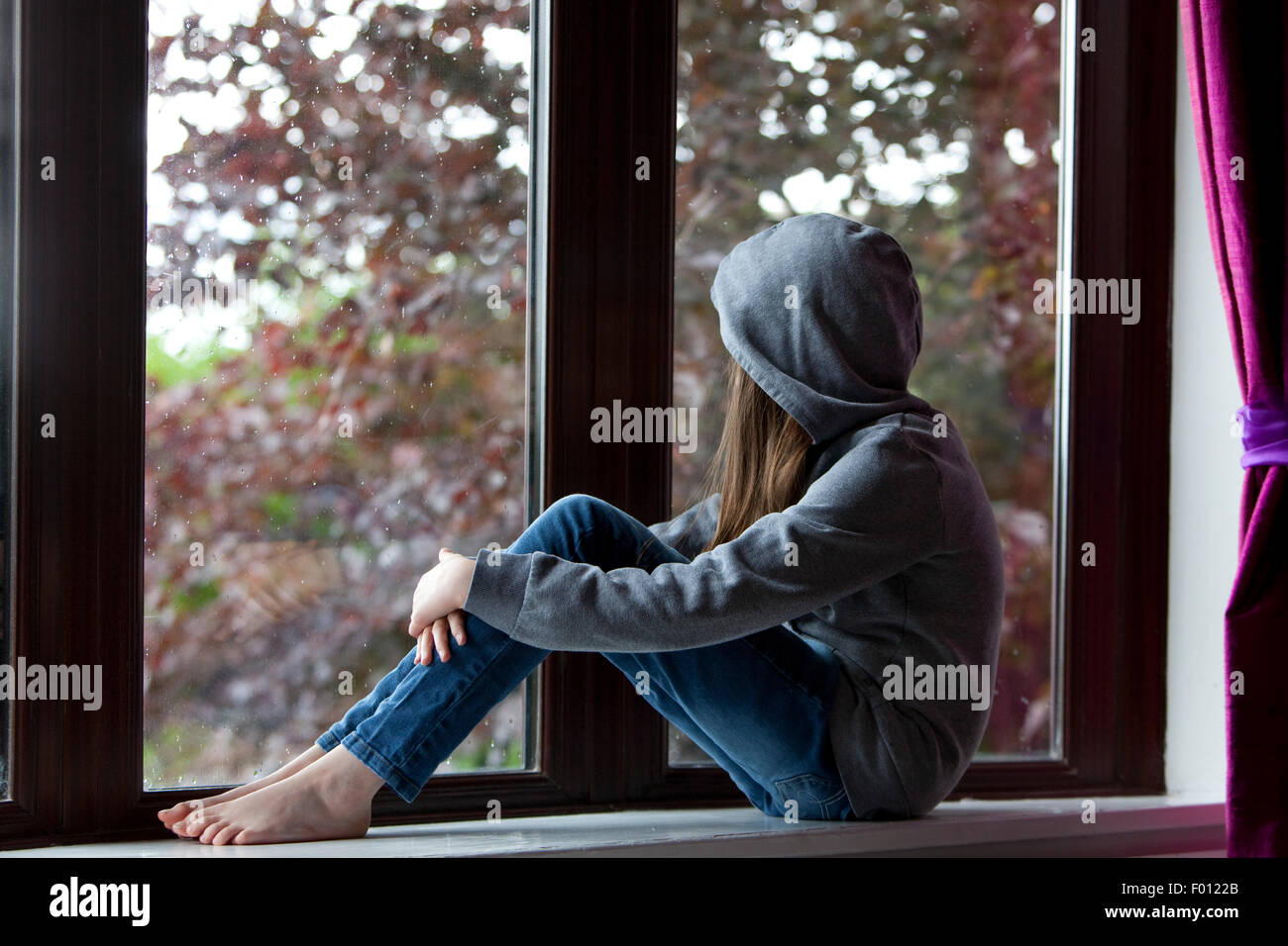 Mädchen in Kapuzen Top und Jeans, sitzt auf einer Fensterbank drinnen und draußen suchen Stockfoto