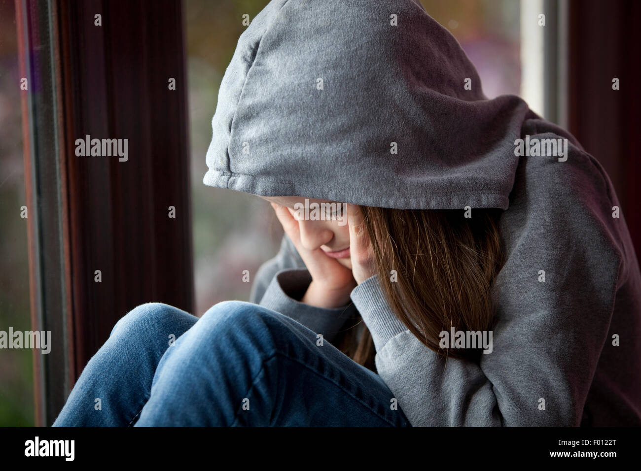 Trauriges Mädchen in Kapuzenshirt, sitzen mit Kopf in Händen in Verzweiflung Stockfoto