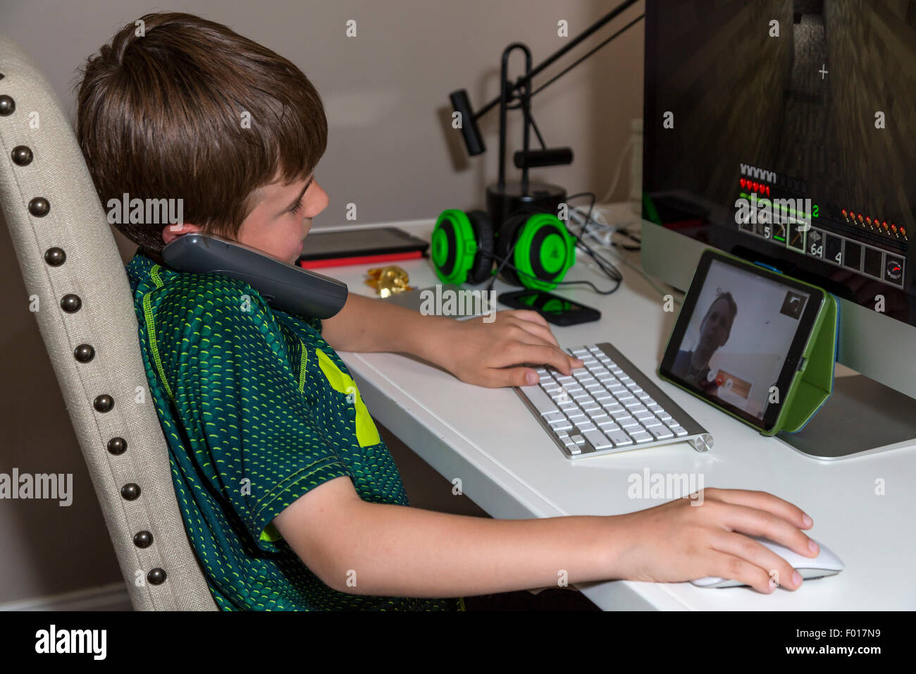 Multitasking beginnt früh.  Young Boy (neun Jahre alt) reden am Telefon während Playing Video Game mit einem anderen jungen über Facetime, Stockfoto