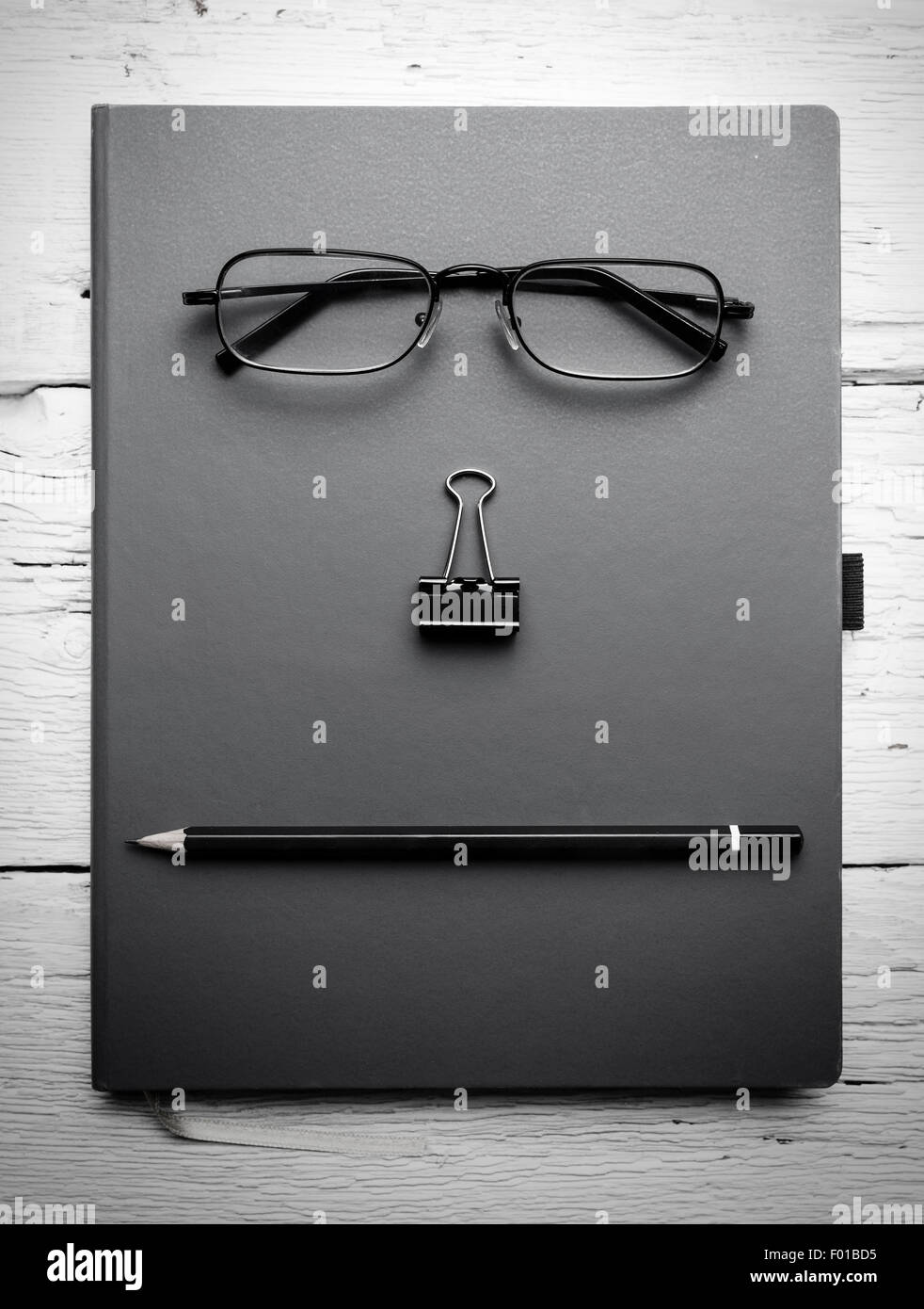 Notizblock, Brillen, Büroklammer und Bleistift auf Holztisch. Schwarz / weiß Foto. Stockfoto