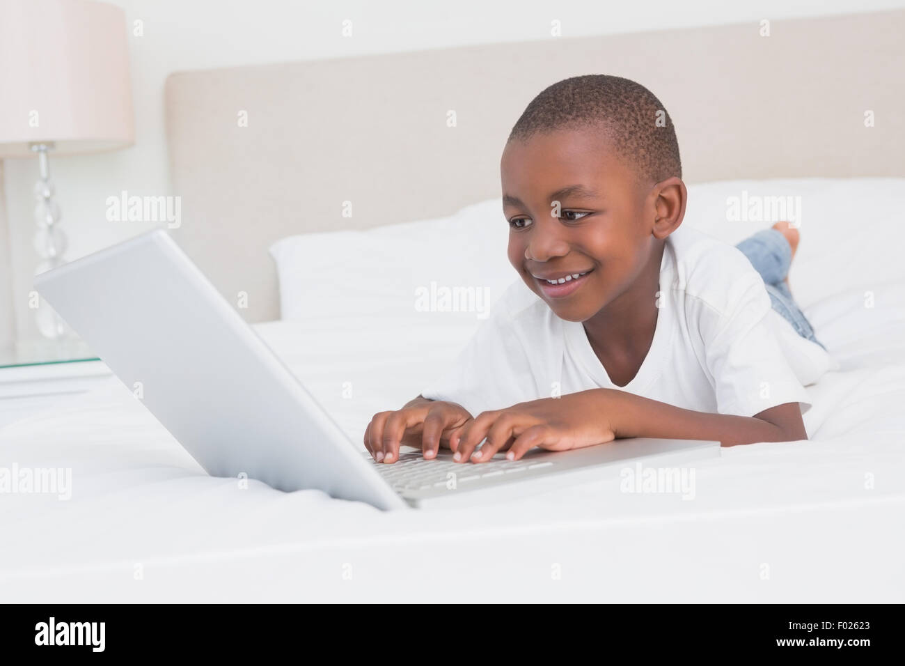 Ziemlich kleiner Junge mit Laptop im Bett Stockfoto