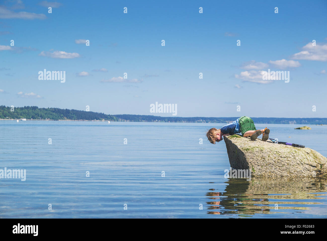 Junge auf einem Felsen blickte auf sein Spiegelbild im Meer Stockfoto