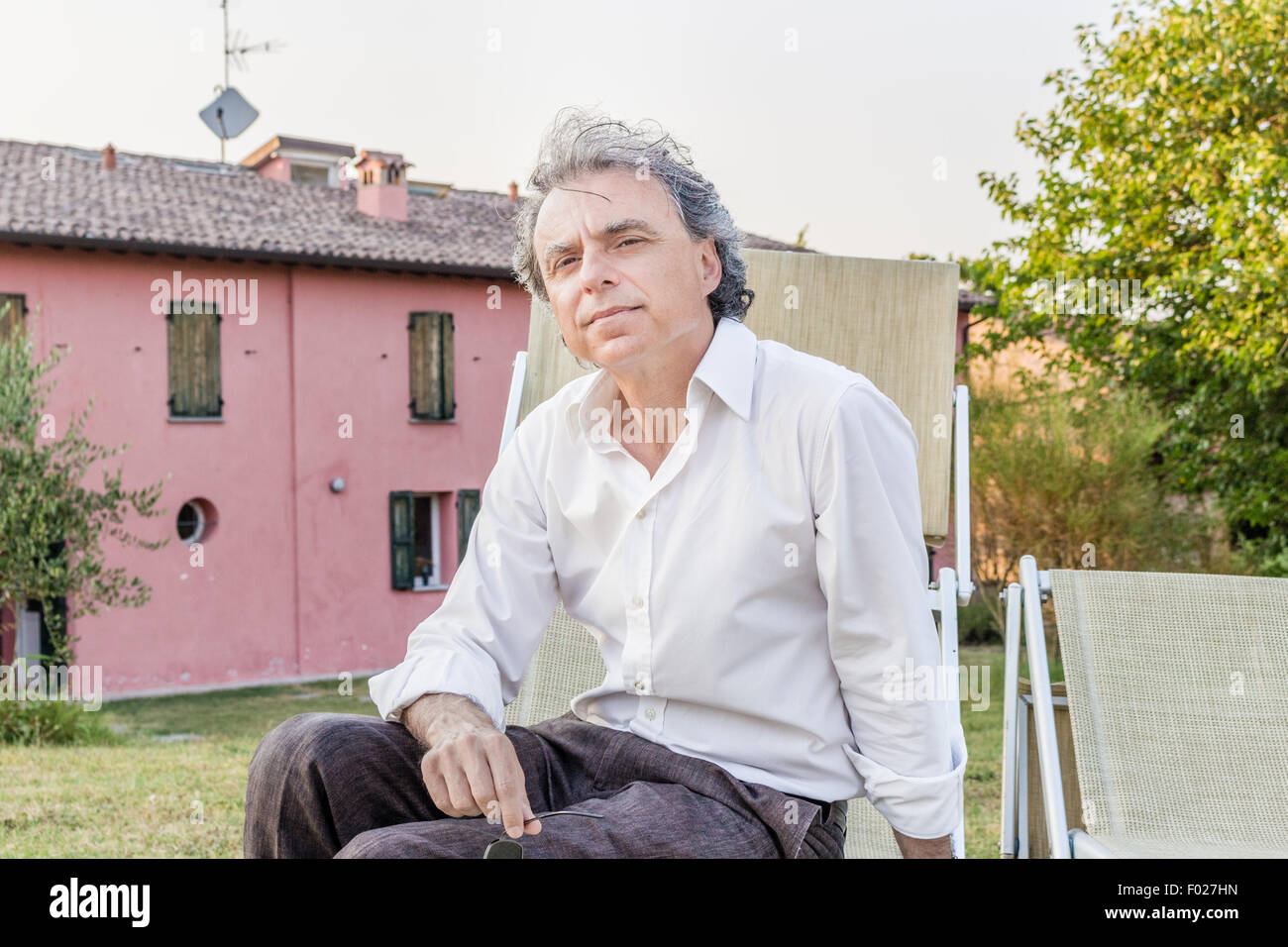 faszinierende wohlhabenden Gentleman von vierzig aus Stadt ruht auf einem Liegestuhl im Garten von einem roten Landhaus in Italien Stockfoto