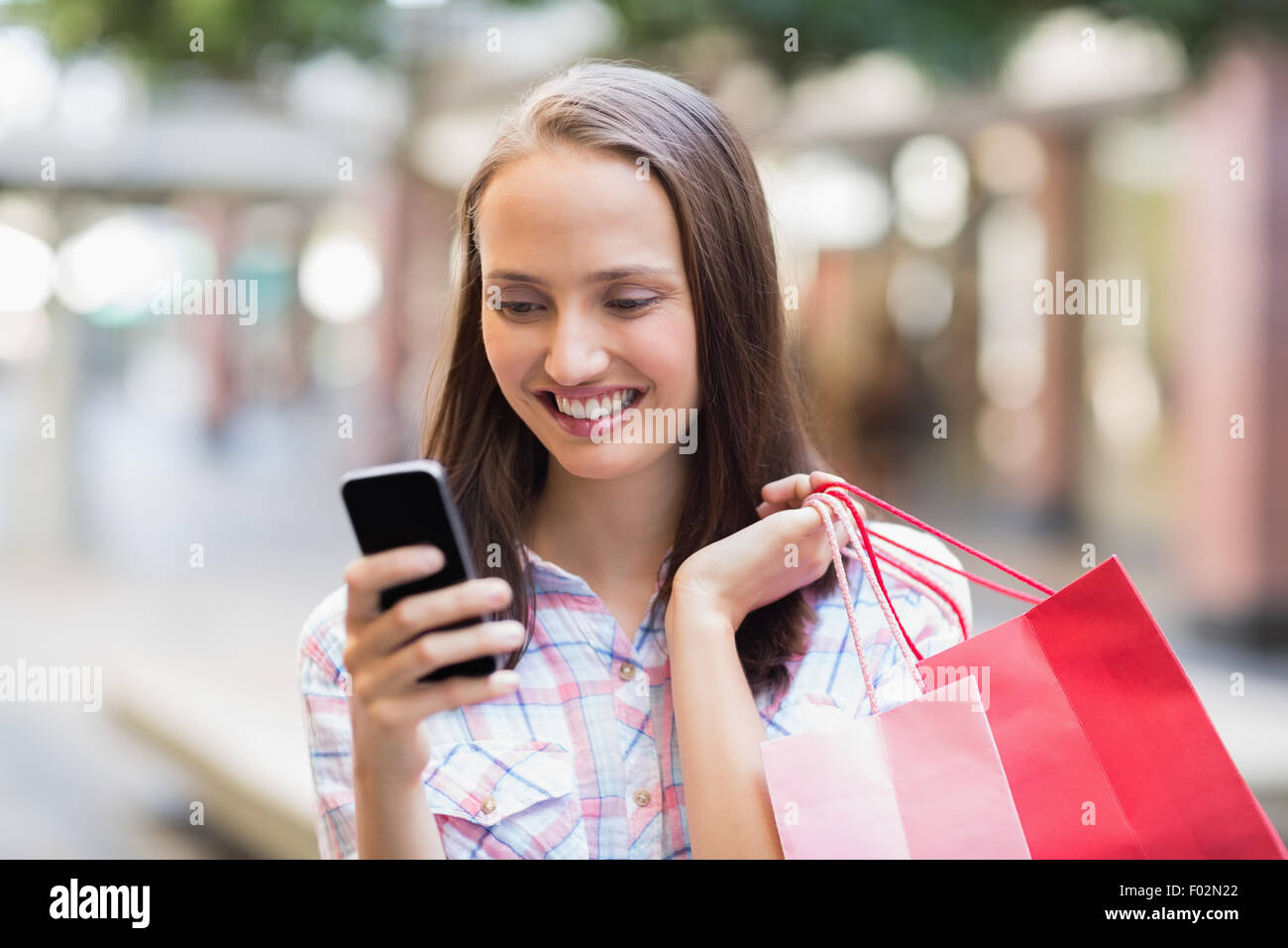 Hübsche Brünette mit ihrem Smartphone und halten Einkaufstasche Stockfoto