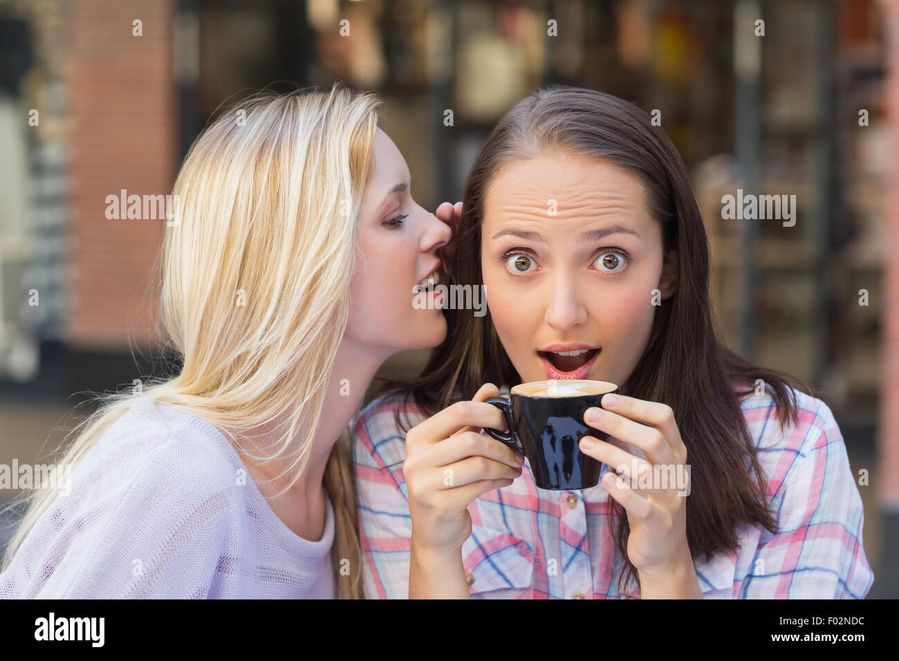 Blonde Frau telling Geheimnis ihrer Freundin beim Kaffeetrinken Stockfoto