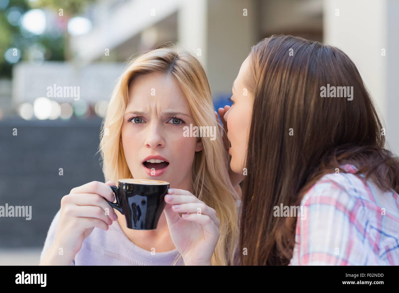 Brünette telling Geheimnis ihrer Freundin beim Kaffeetrinken Stockfoto
