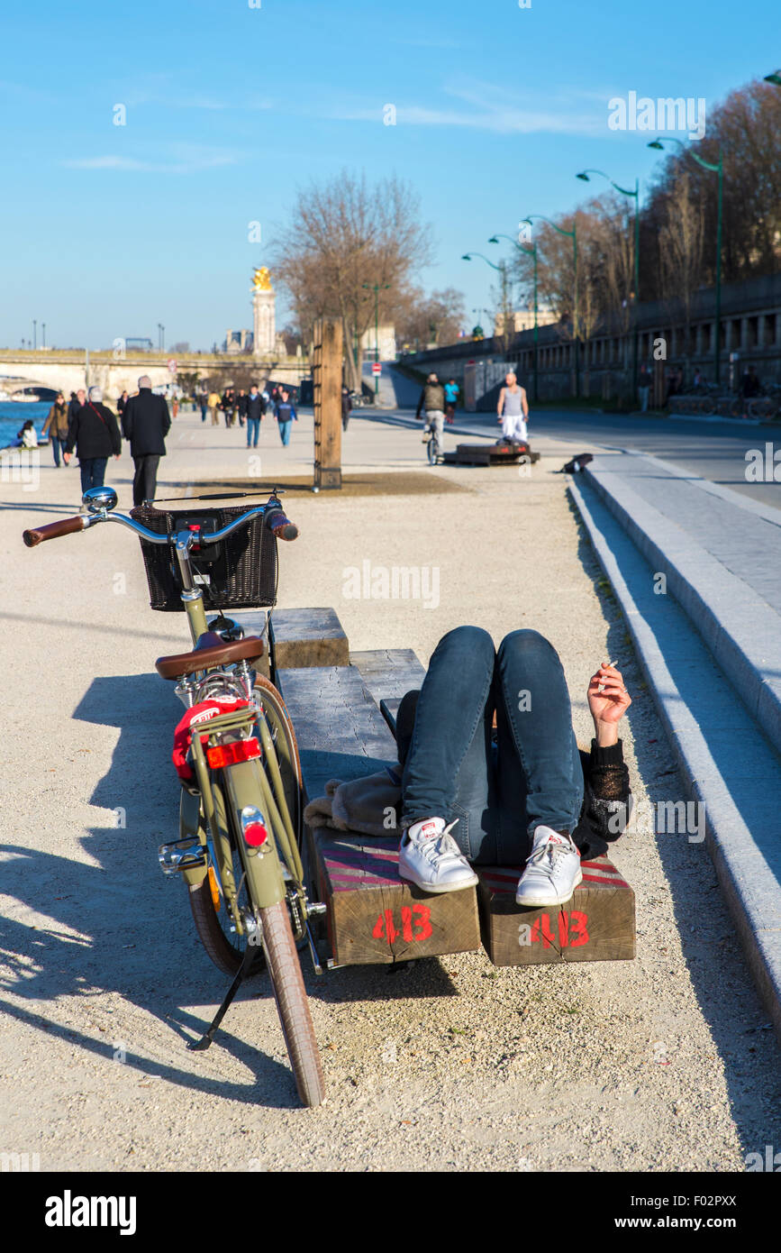 Frau liegend auf Bank am Ufer der Seine, Pont des Invalides Brücke hinter Paris Stockfoto