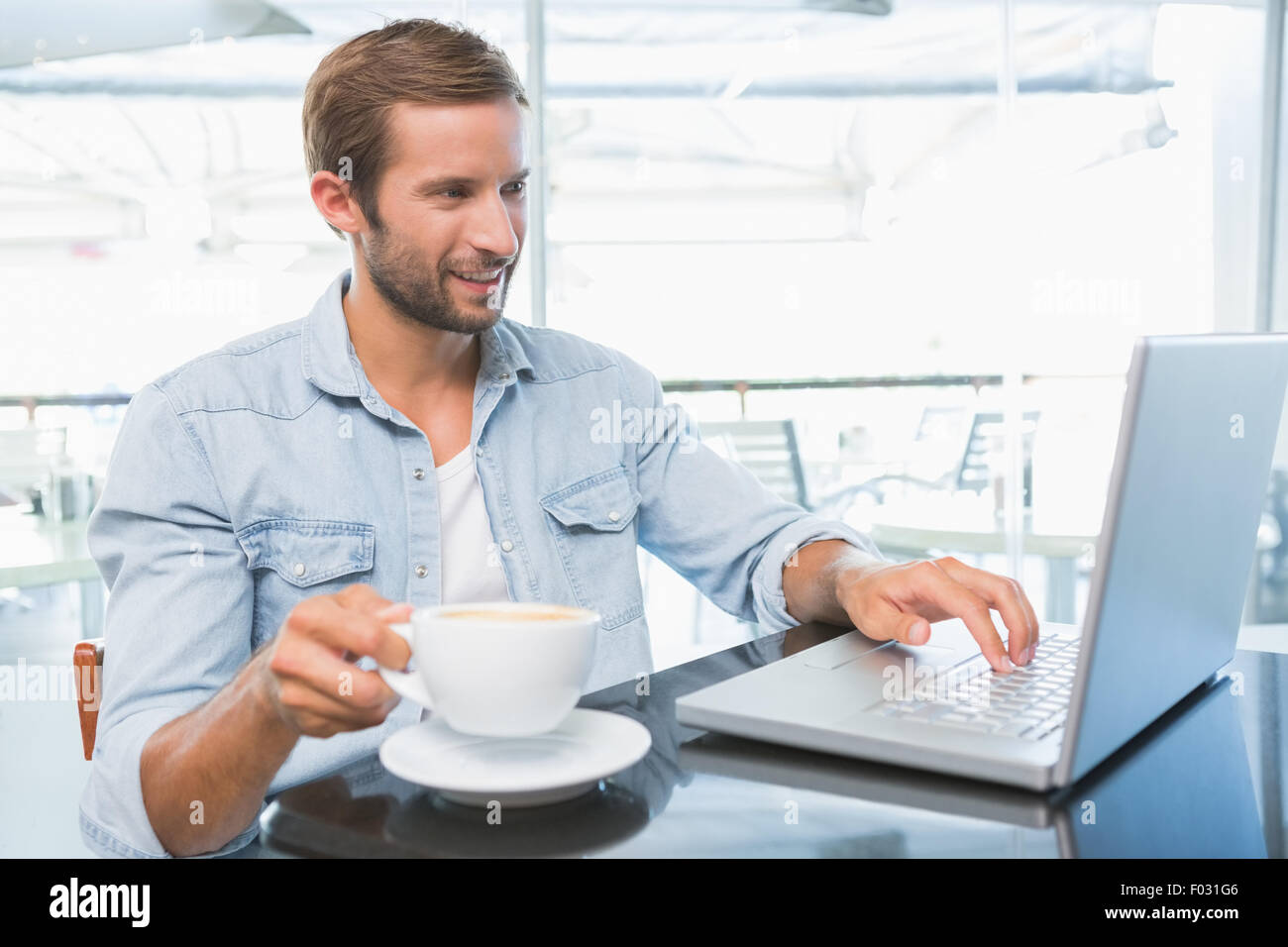 Glücklich Jüngling mit gedrückter seinen Kaffee auf dem Laptop eingeben Stockfoto