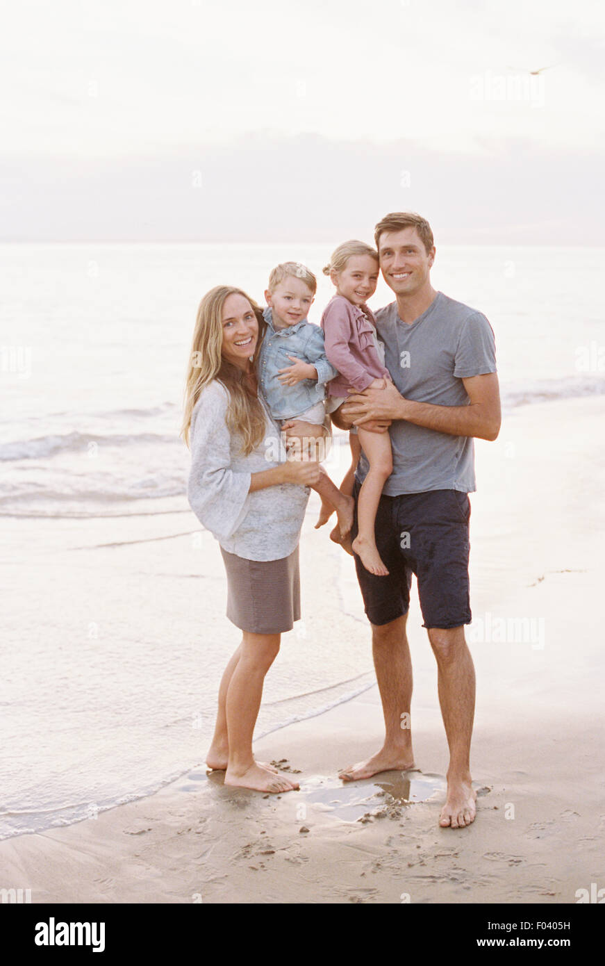 Paar steht mit ihrem Sohn und Tochter an einem Sandstrand am Meer, Blick in die Kamera, lächelnd. Stockfoto