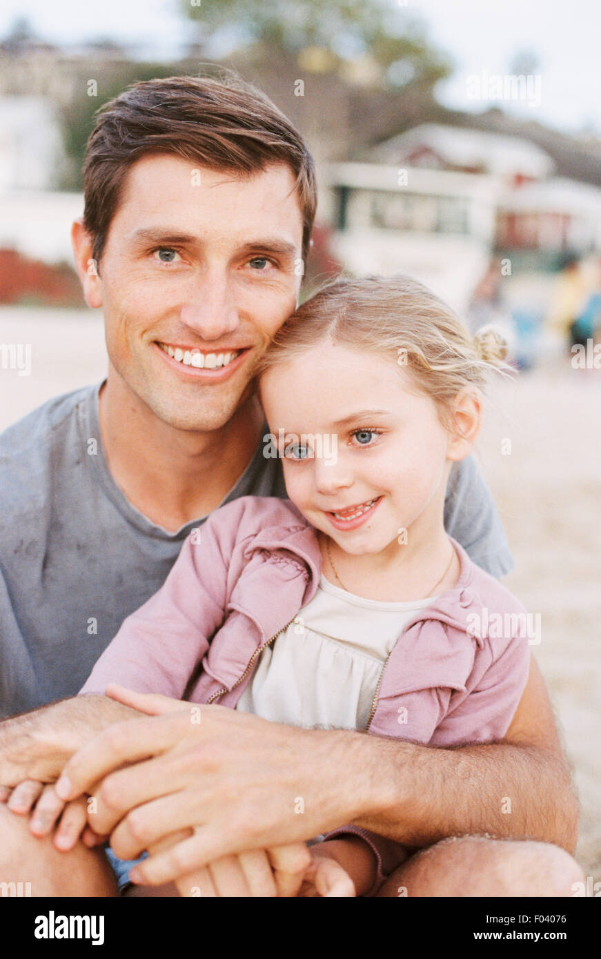 Junges Mädchen auf ihres Vaters Schoß, Blick in die Kamera, lächelnd. Stockfoto