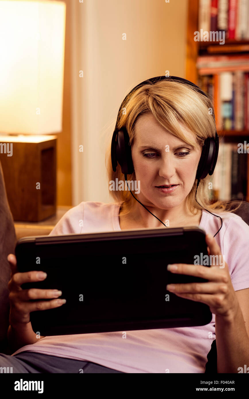 Frau mit Tablet und Kopfhörer zu Hause auf sofa Stockfoto