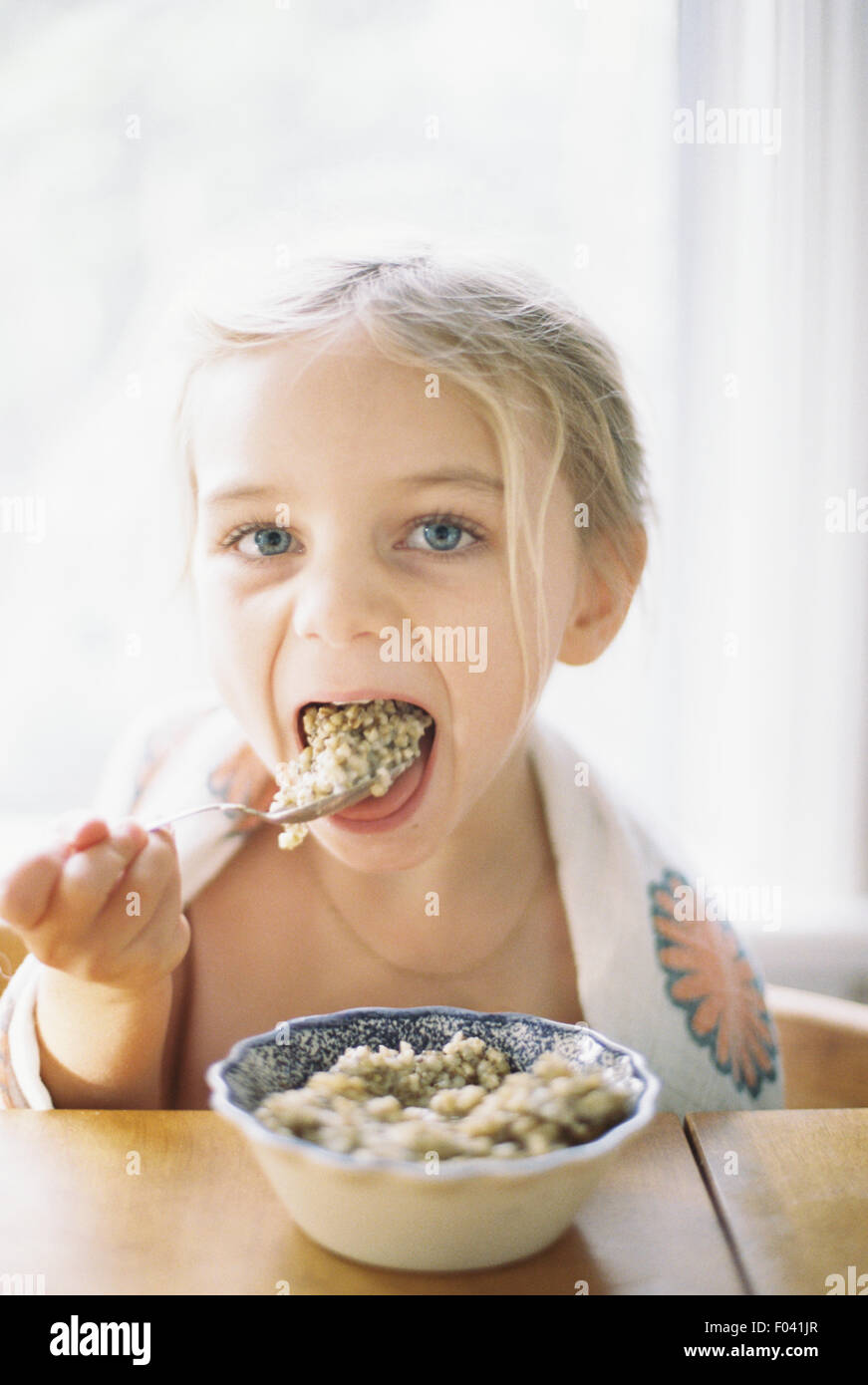 Junges Mädchen an einem Tisch sitzen Frühstück aus einer Schüssel essen. Stockfoto