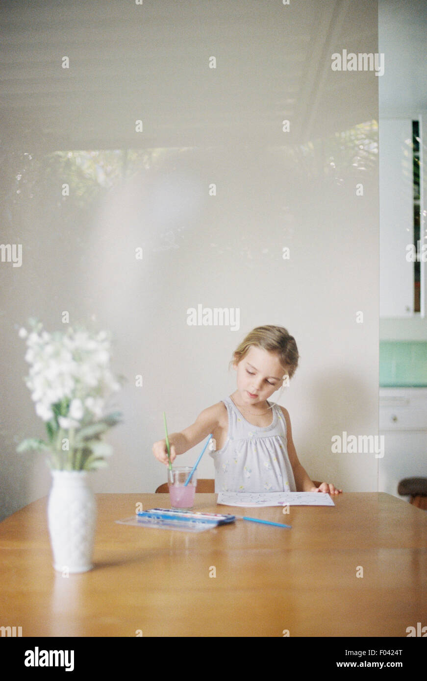 Junges Mädchen saß an einem Tisch, Malerei, eine Vase mit weißen Blüten. Stockfoto