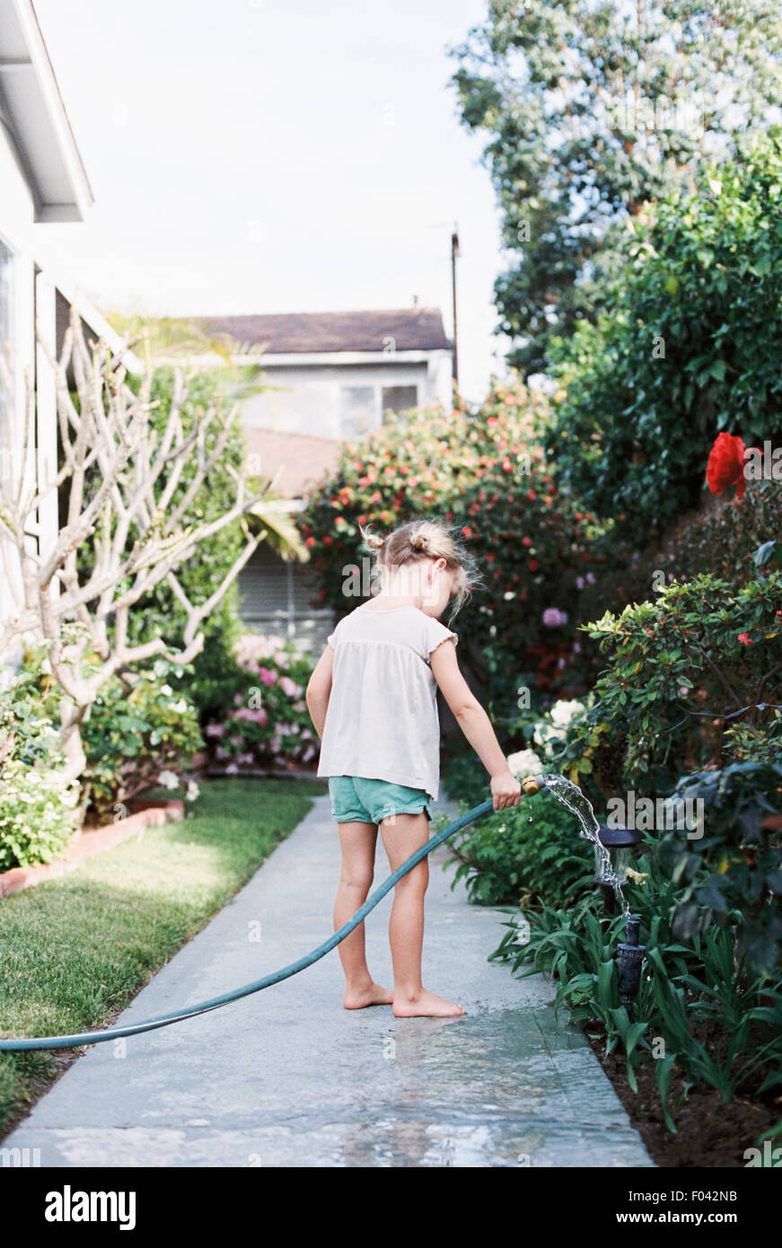 Junges Mädchen auf einen Pfad in einem Garten stehen, spielen mit einem Wasserschlauch. Stockfoto