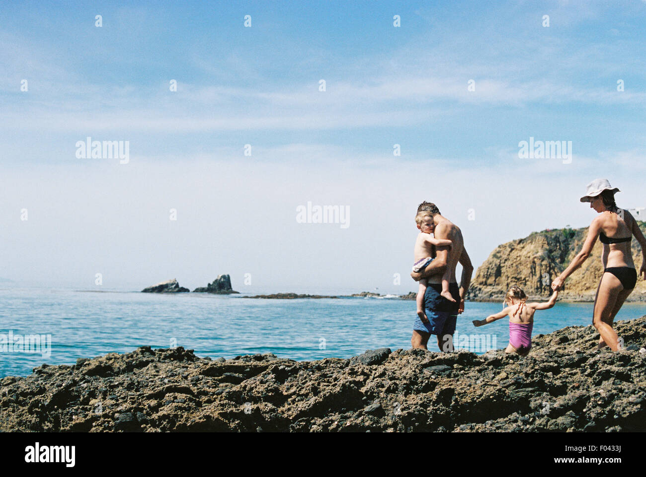 Eine Familie auf Urlaub, zwei Erwachsene mit ihrem Sohn und Tochter, die zu Fuß über Felsen am Meer. Stockfoto