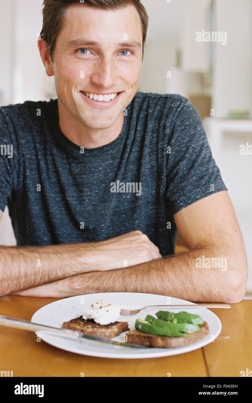 Man sitzt vor einem Teller mit Essen an einem Tisch mit Blick in die Kamera, lächelnd. Stockfoto