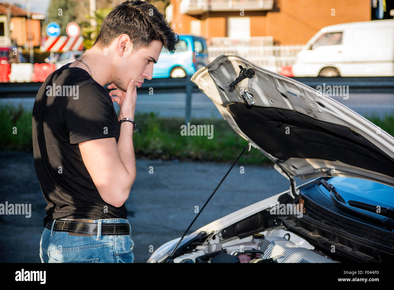 Hübscher junger Mann versucht, einen Automotor, reparieren Blick in offene Motorhaube Stockfoto
