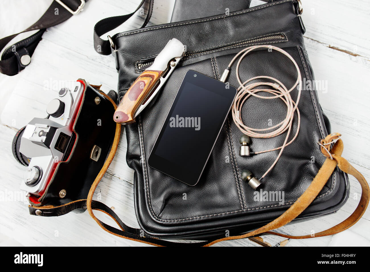 Objekte auf hölzernen Hintergrund: Leder Tasche, Kamera, Smartphone, Schlüssel, Messer. Outfit des jungen Mannes. Stockfoto