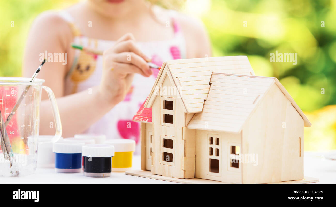 Kleine Mädchen malt Holzmodell des Hauses, Sommer im Freien, neues Wohnkonzept Stockfoto