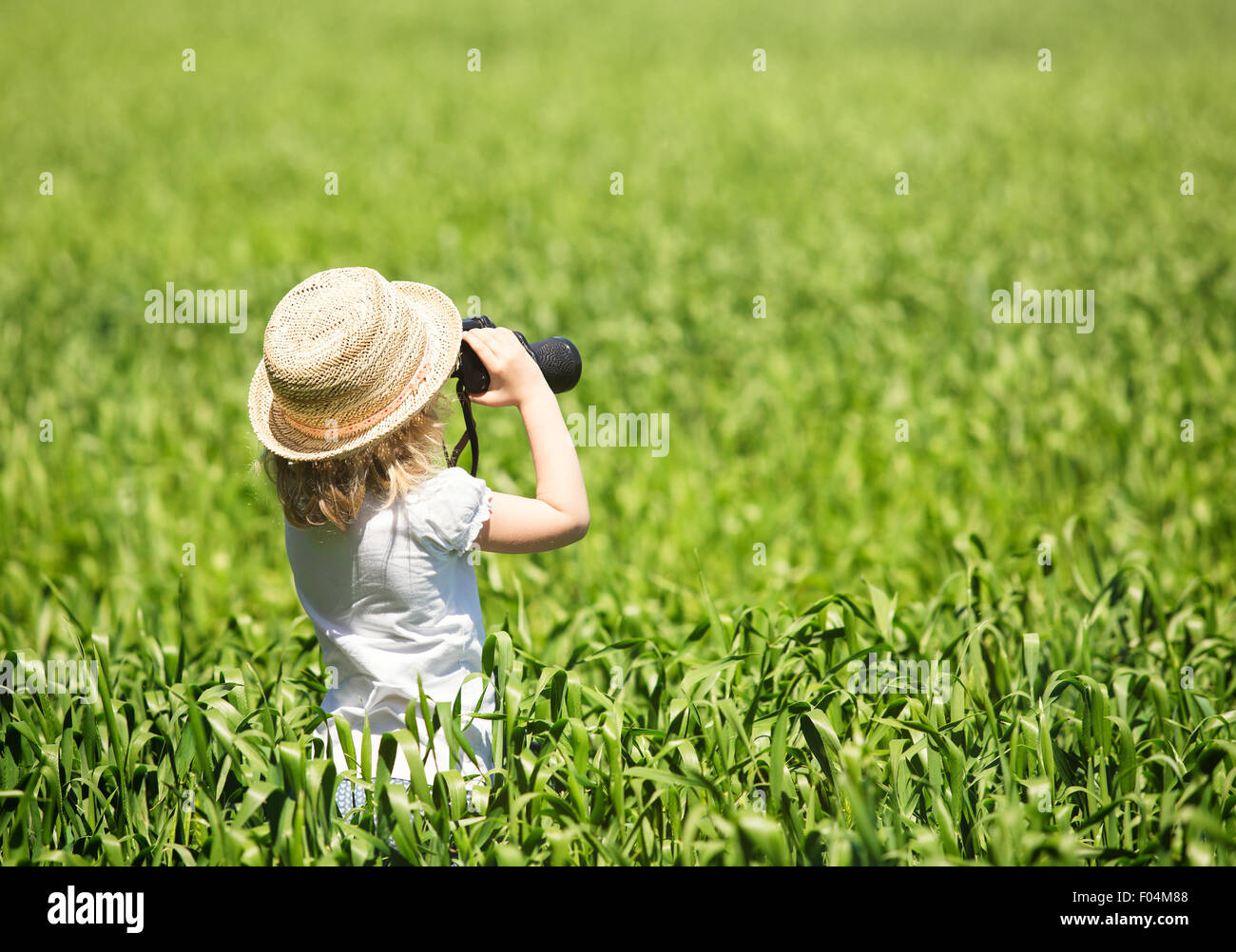 Kleine blonde Mädchen in Strohhut Blick durch ein Fernglas outdoor Stockfoto