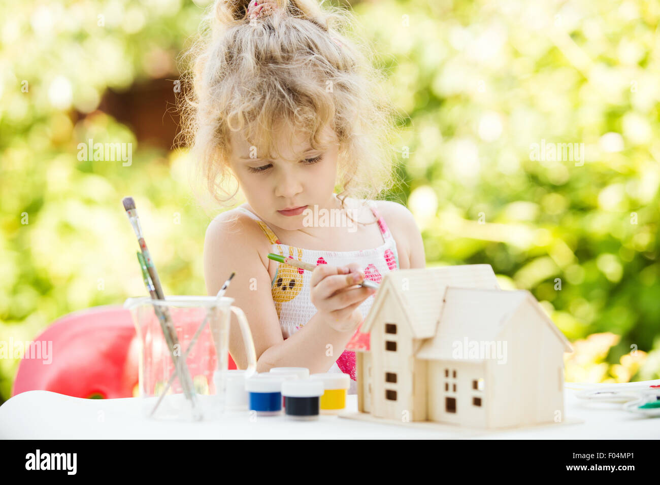 Porträt von kleinen Mädchen malt Holzmodell des Hauses, Sommer im Freien, neues Wohnkonzept Stockfoto