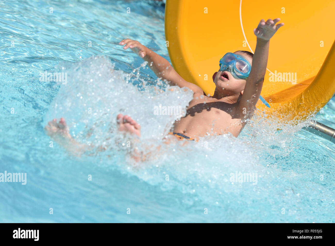 Ailingen Sie, Deutschland. 7. August 2015. Kleiner Junge Georgios gleitet nach unten eine Wasserrutsche und spritzt in das Refereshing Wasser am Freibad Poool mit Wellenbad Ailingen, Deutschland, 7. August 2015. Foto: Felix Kaestle/Dpa/Alamy Live News Stockfoto