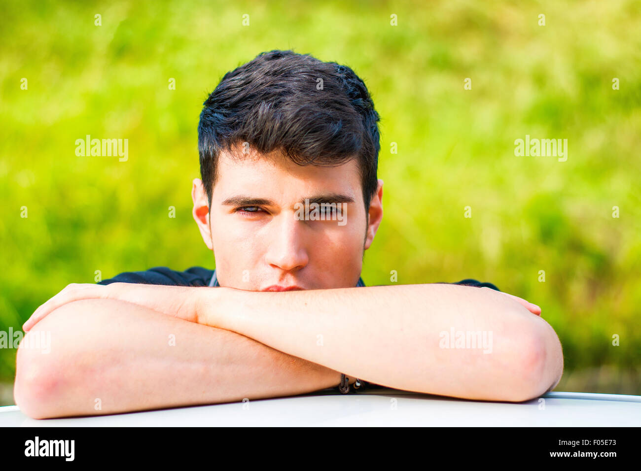 Kopf und arme Schuss von hübscher attraktiver junger Mann, Blick in die Kamera im Freien, stützte sich auf flache Oberfläche mit Kopf auf Seite Stockfoto