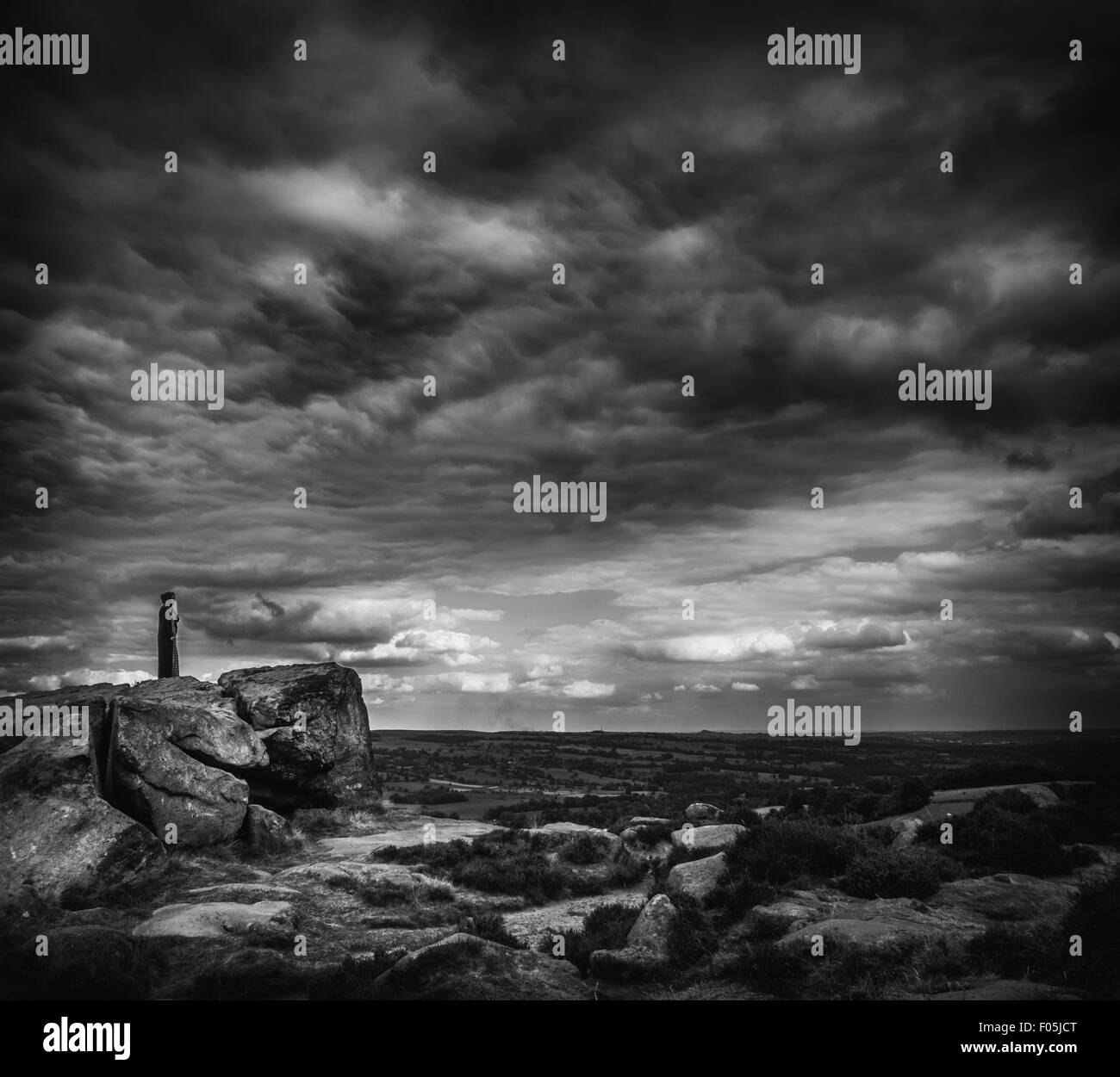 Dramatische Bild eines caped Frau steht auf Felsen mit einer weitläufigen Landschaft Landschaft und Moody sky Stockfoto