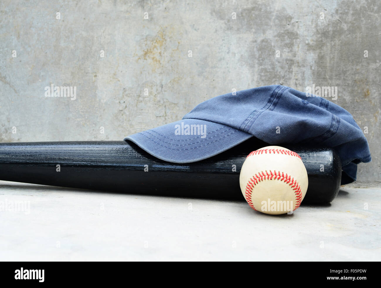 Baseballschläger und Kappe gegen eine Betonwand als Hintergrund Stockfoto