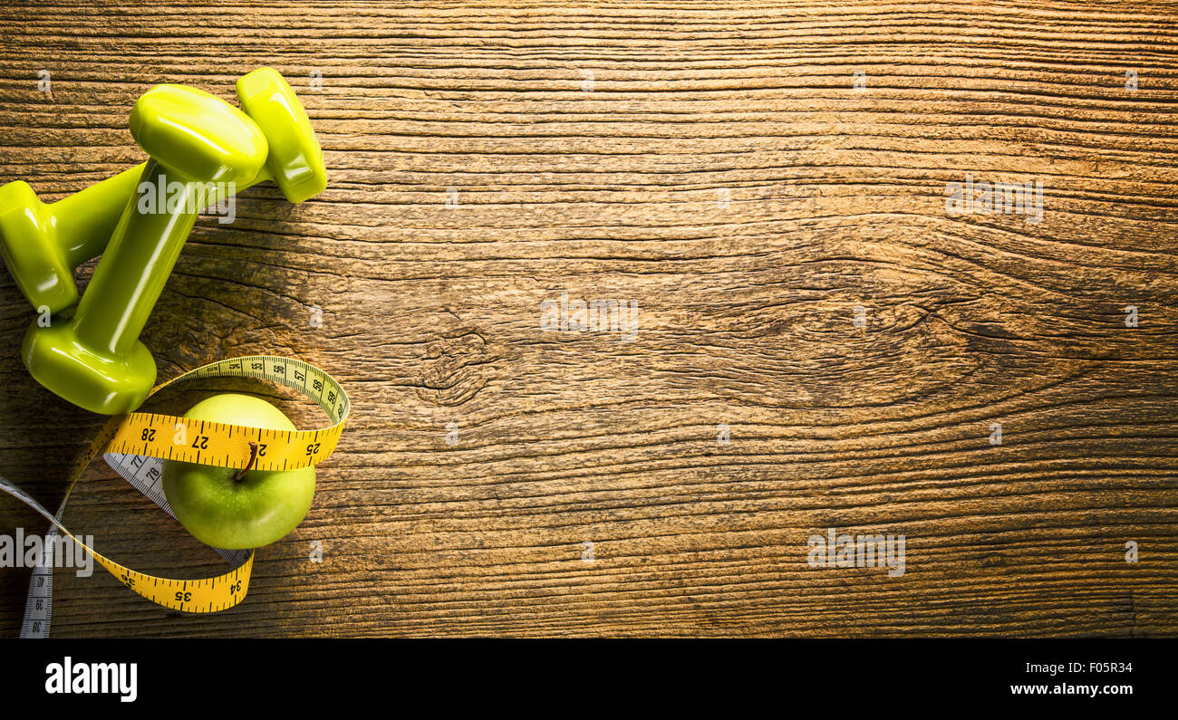Zwei Kurzhanteln, grüner Apfel, Maßband auf hölzernen Hintergrund Stockfoto