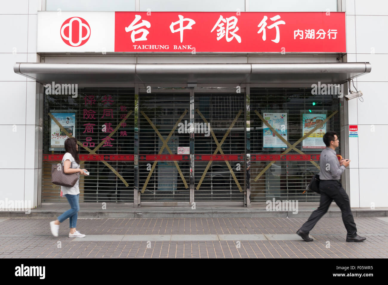 Taipei, Taiwan, 7. August 2015. Ein Mann und eine Frau gehen von einer Bank in Taipei, die für den Ansturm der Taifun Soudelor vorbereitet hat, durch Abkleben der Schaufenster, eine gängige Praxis in Taiwan. Taifun Soudelor übergangen Taiwan am 7. August und 8. Bildnachweis: Perry Svensson/Alamy Live-Nachrichten Stockfoto