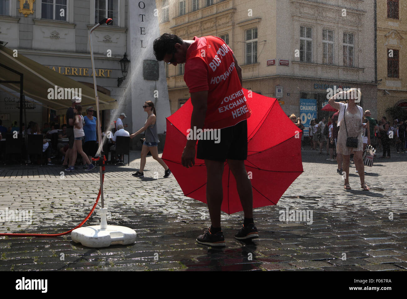 Prag, Tschechische Republik. 7. August 2015. Ein Mann arbeitet als menschliche Plakatwand und halten einen roten Regenschirm versucht, von einer Wasser-Sprinkler installiert am Altstädter Ring an einem extrem heißen Tag in Prag, Tschechische Republik, am 7. August 2015 abzukühlen. In die letzten Tagen, die der Tschechischen Republik von Hitzewellen als Tagestemperaturen getroffen wurde erreicht bis zu 40 Grad Celsius (104 Grad Fahrenheit). Stockfoto