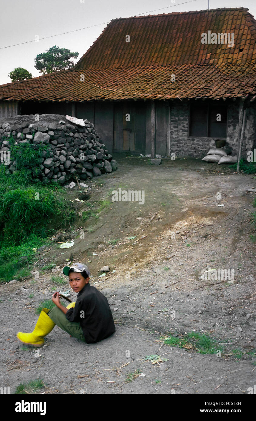 Ein Kind, das auf einer Landstraße sitzt, im Hintergrund eines Hauses in Selo, am Fuße des Berges Merapi in Boyolali, Zentraljava, Indonesien. Stockfoto