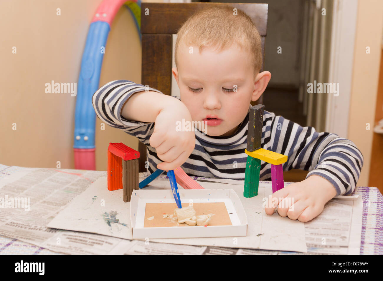 der kleine Junge sitzt an einem Tisch und beschäftigt sich ein Formteil aus Plastilin Stockfoto