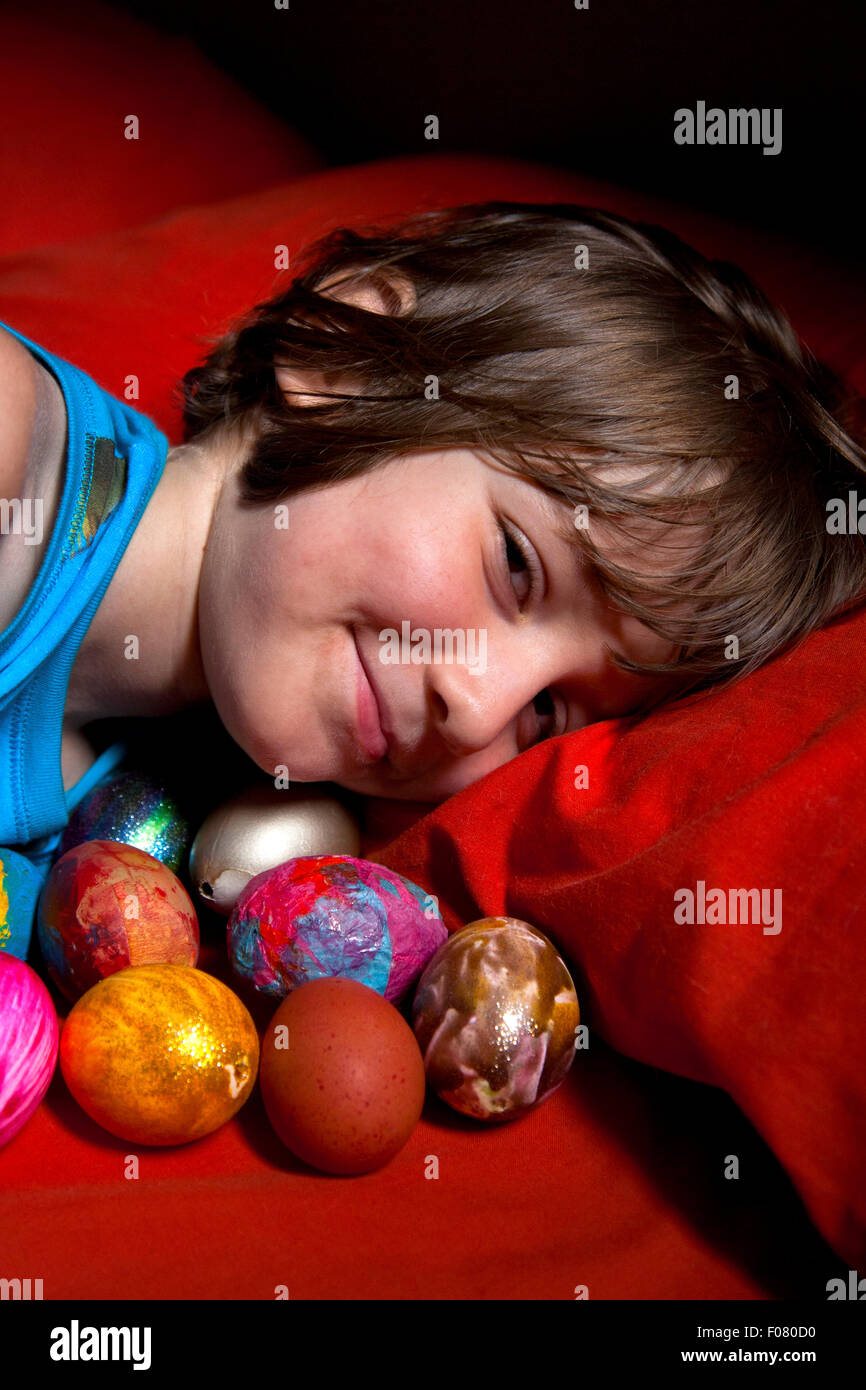 6 Jahre alter Junge im Bett mit seiner Sammlung von bemalten Eiern liegen. Stockfoto