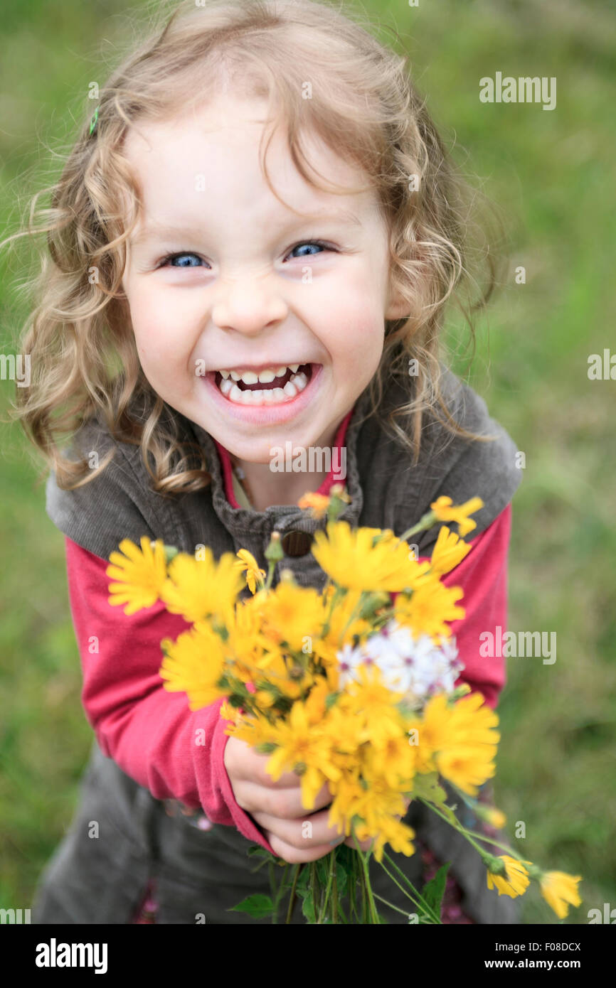 Glückliches Babymädchen spielen im Freien, niedlichen Kind halten frische Blumen Stockfoto