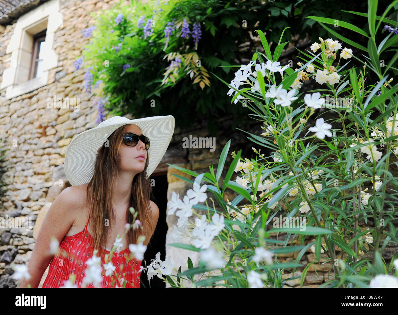 Junge schöne Frau in ihren 20ern tragen große Krempe Sonnenhut schnüffeln Blumen außerhalb ihrer Urlaub Ferienhaus Frankreich Stockfoto