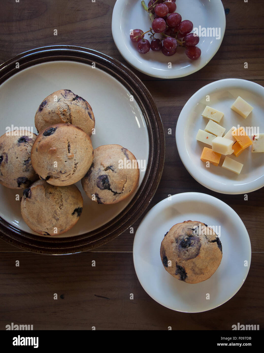Mehrere Platten mit Blaubeer-Muffins, sitzen Käsewürfel und rote kernlose Trauben auf eine braune hölzerne Tischplatte. Stockfoto